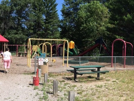 Picnic table next to fenced in play ground equipment including swings, tire swings, slides and sandbox.